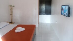 Una habitación de hotel con una cama, televisor, planta de bambú y una puerta que da a otra habitación.