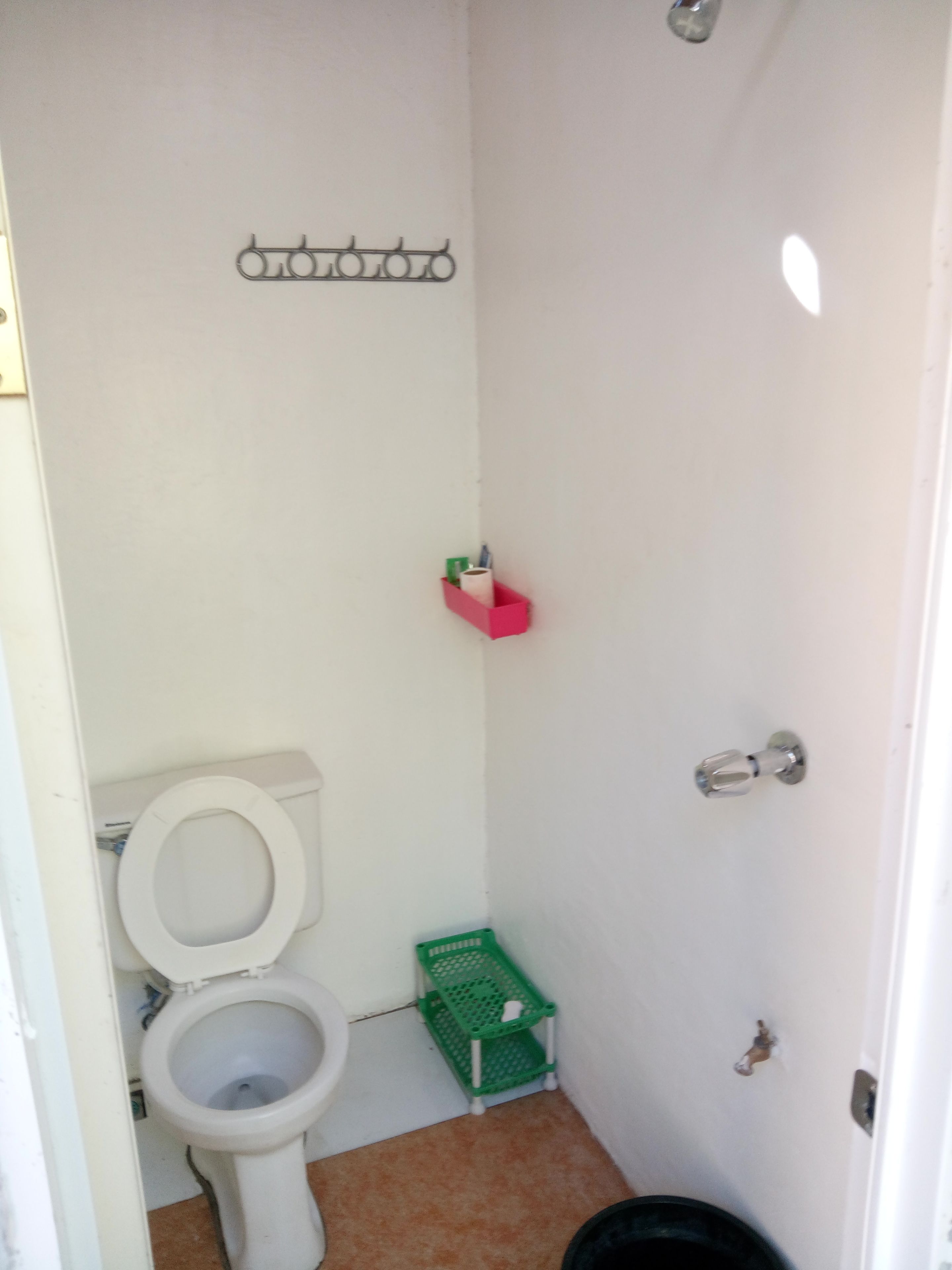 Un baño pequeño y blanco con un inodoro, una cesta verde y un caja de almacenamiento rosa.