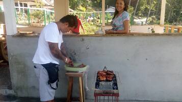 A man grilling meat on a portable grill outside a building with a woman standing nearby.