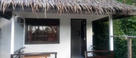 A small house with a thatched roof, a wooden bench, and a door leading to an interior space.