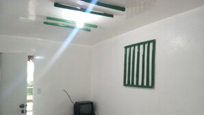 Una habitación con televisión sobre un escritorio, una silla y una ventana con un persiano verde.