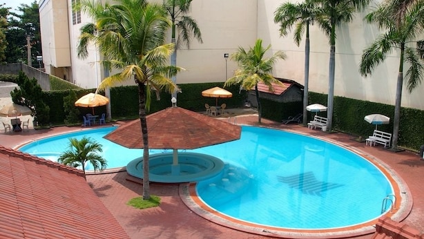 Una piscina con palmeras, sillas de descanso y sombrillas.
