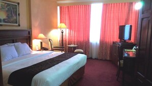Una habitación de hotel con una cama grande, un escritorio con ordenador, una silla, una lámpara y un cuadro en la pared.