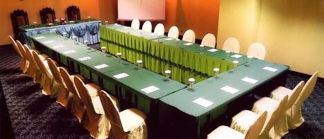 Un salón de conferencias con una larga mesa, sillas, una pantalla de proyector y un cartel de 'No Fumar'.