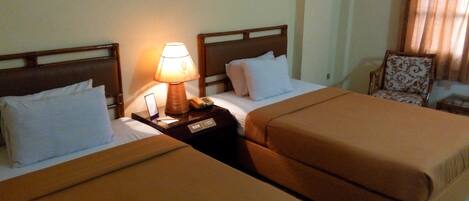 A hotel room with two beds, a nightstand with a lamp, a chair, and a painting on the wall.
