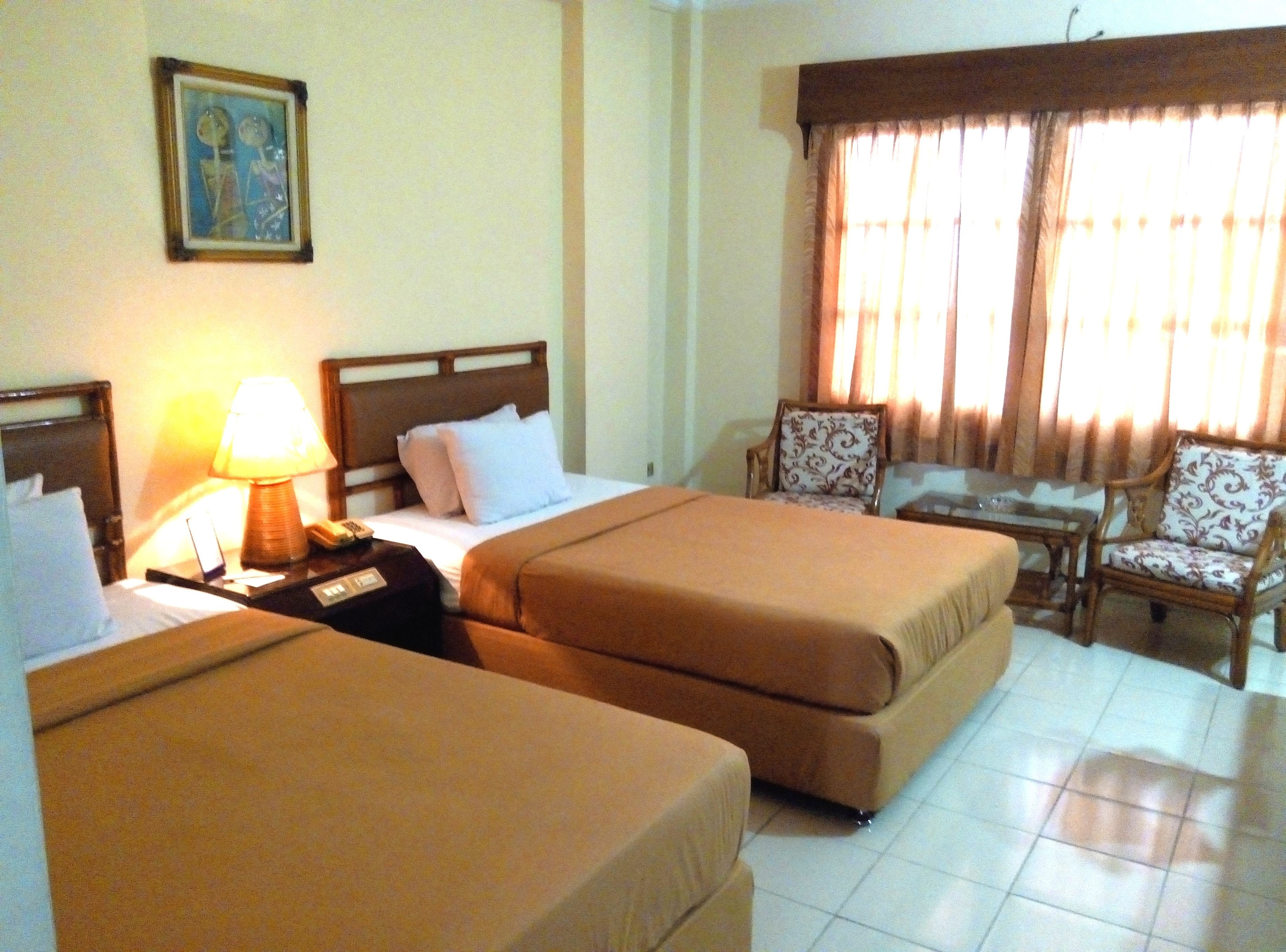 A hotel room with two beds, a desk, a chair, and a lamp.
