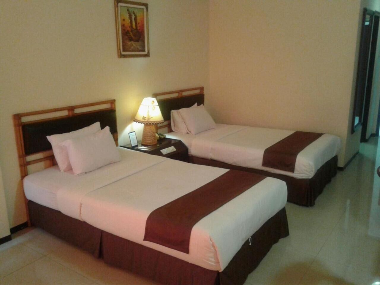 A hotel room with two beds, a nightstand with a lamp, and a painting on the wall.