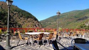 An outdoor patio with stone flooring, tables, and chairs, overlooking a mountainous landscape.