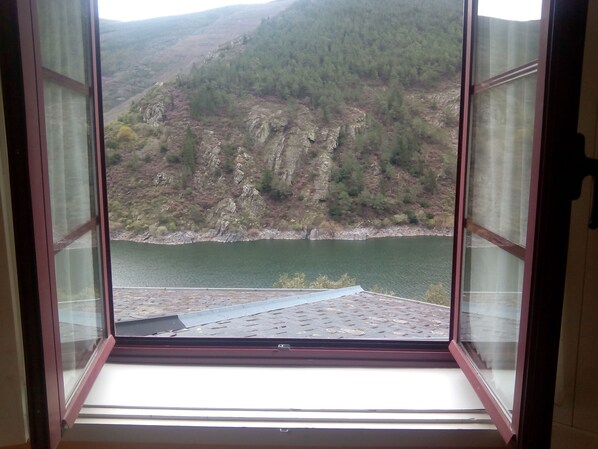 Une vue depuis une fenêtre donnant sur un toit en métal, avec en contrebas un lac et une colline boisée.