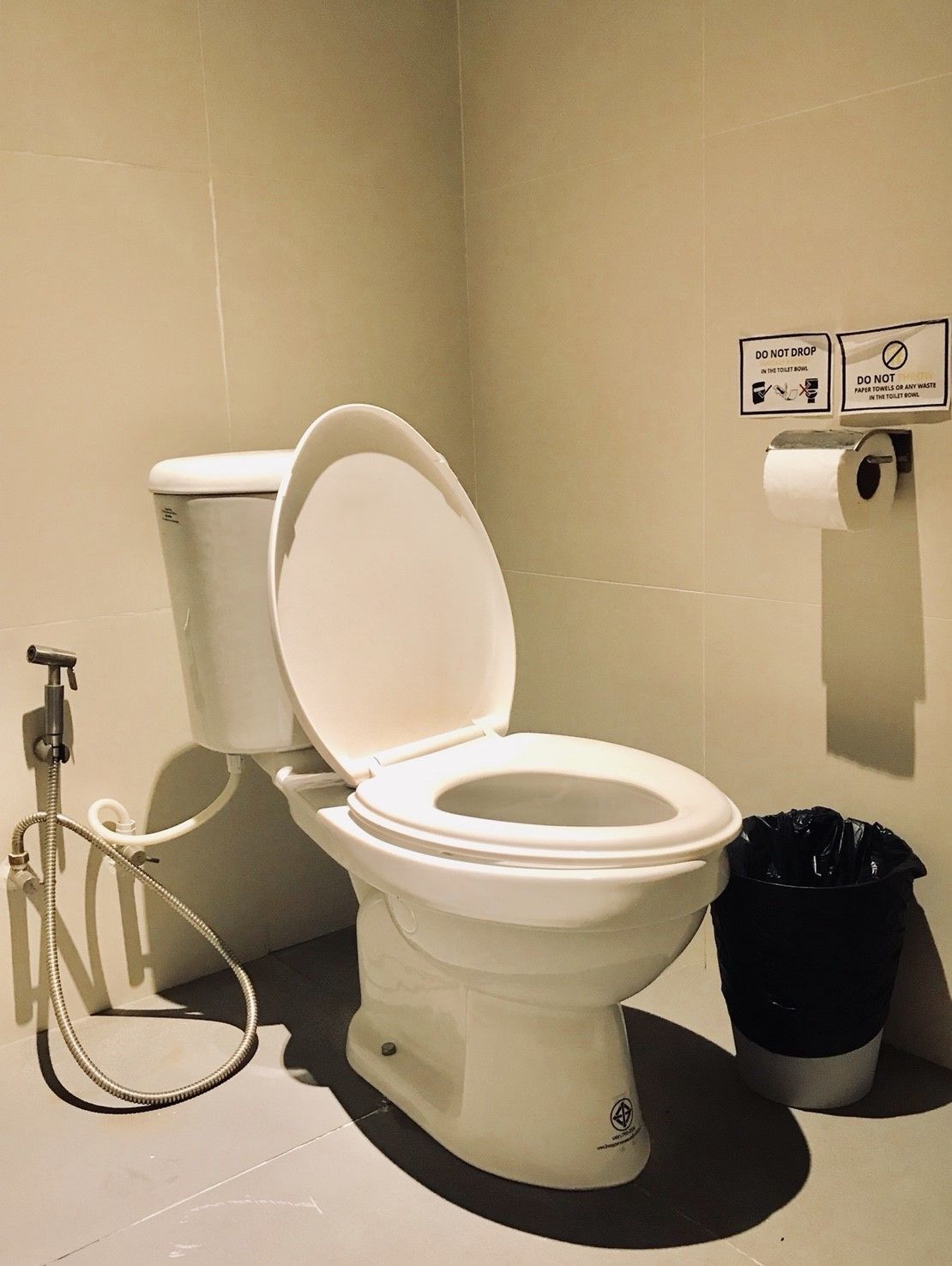 A toilet with a bidet attachment, a paper towel dispenser, and a trash bin.