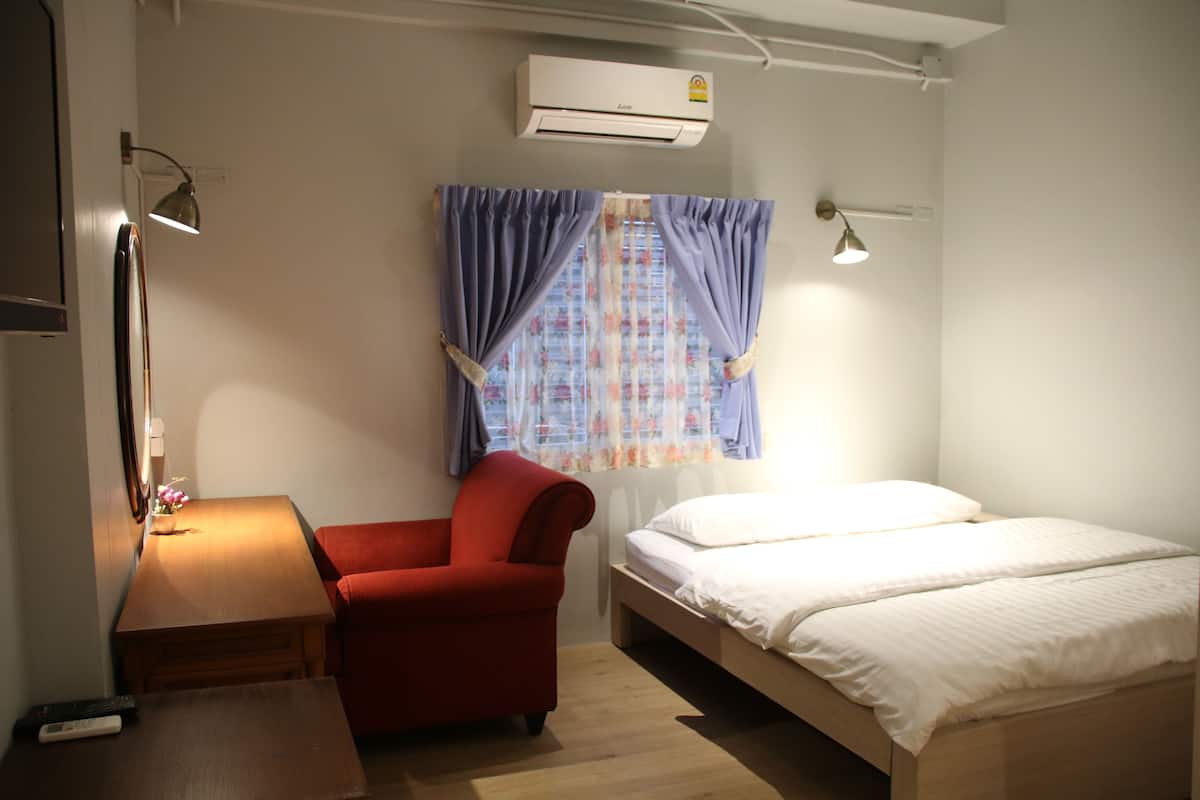 A bedroom with a single bed, a red chair, a wooden table, and a desk lamp.