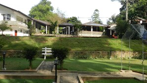 A residential area with houses, a grassy lawn, a pathway, and a small garden with a bench. - Eeescart Family Resort (Bandarawela)