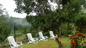 A garden with four white lounge chairs arranged in a semi-circle, surrounded by lush greenery and a stone pathway. - Eeescart Family Resort (Bandarawela)