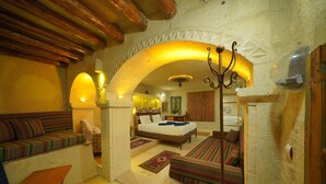 A cozy room with a bed, a sofa, and a small table. There is a decorative archway and a chandelier. - Fosil Cave Hotel (Ürgüp)