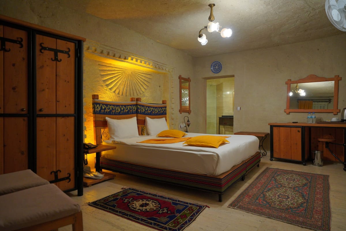 Un dormitorio con cama, mesitas de noche, un armario, un espejo y una alfombra estampada.