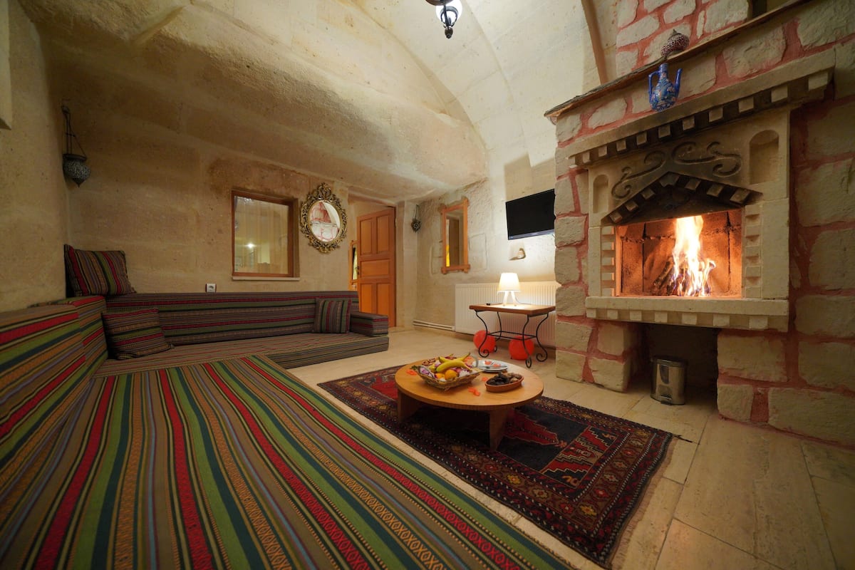 Una sala de estar acogedora con chimenea de piedra, un sofá a rayas y una mesa de centro con fruta.