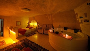 A dimly lit room with a large bathtub, a sofa, and a small table with a candle and wine glasses. - Fosil Cave Hotel (Ürgüp)