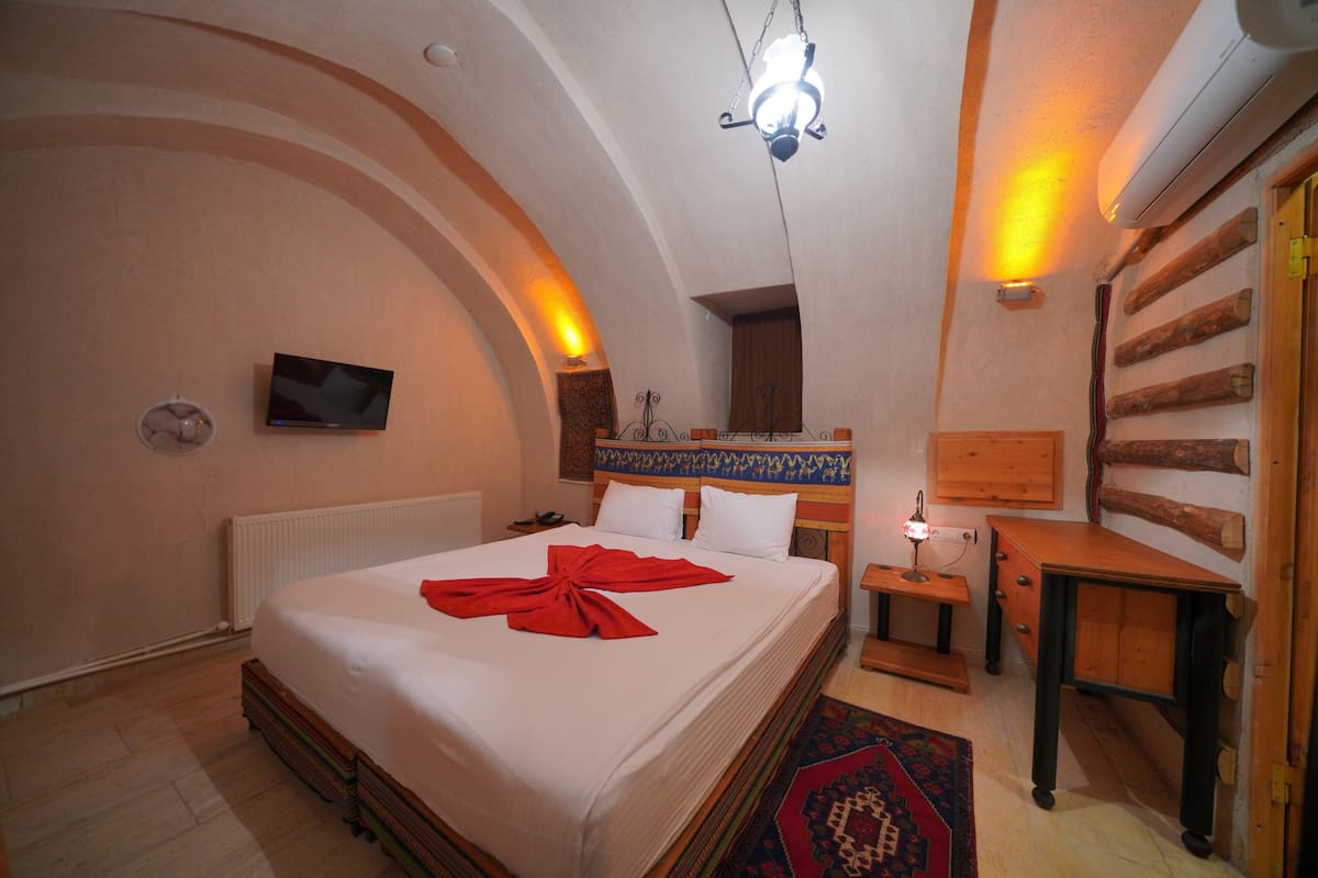 Una habitación de hotel con una cama grande, un televisor, una mesita de noche de madera y un calefactor instalado en la pared.