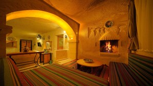 A cozy room with a fireplace, a bed with a striped blanket, and a small table with a bowl. - Fosil Cave Hotel (Ürgüp)
