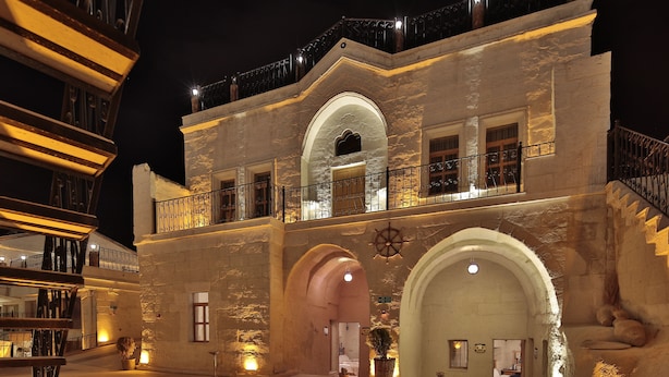 A historic building with a stone facade, arched entrances, and a balcony with railings. - Fosil Cave Hotel (Ürgüp)