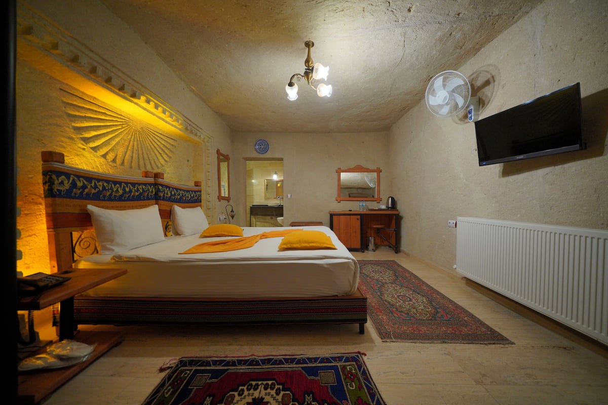 Un dormitorio con cama, escritorio, silla, televisor, espejo y radiador.