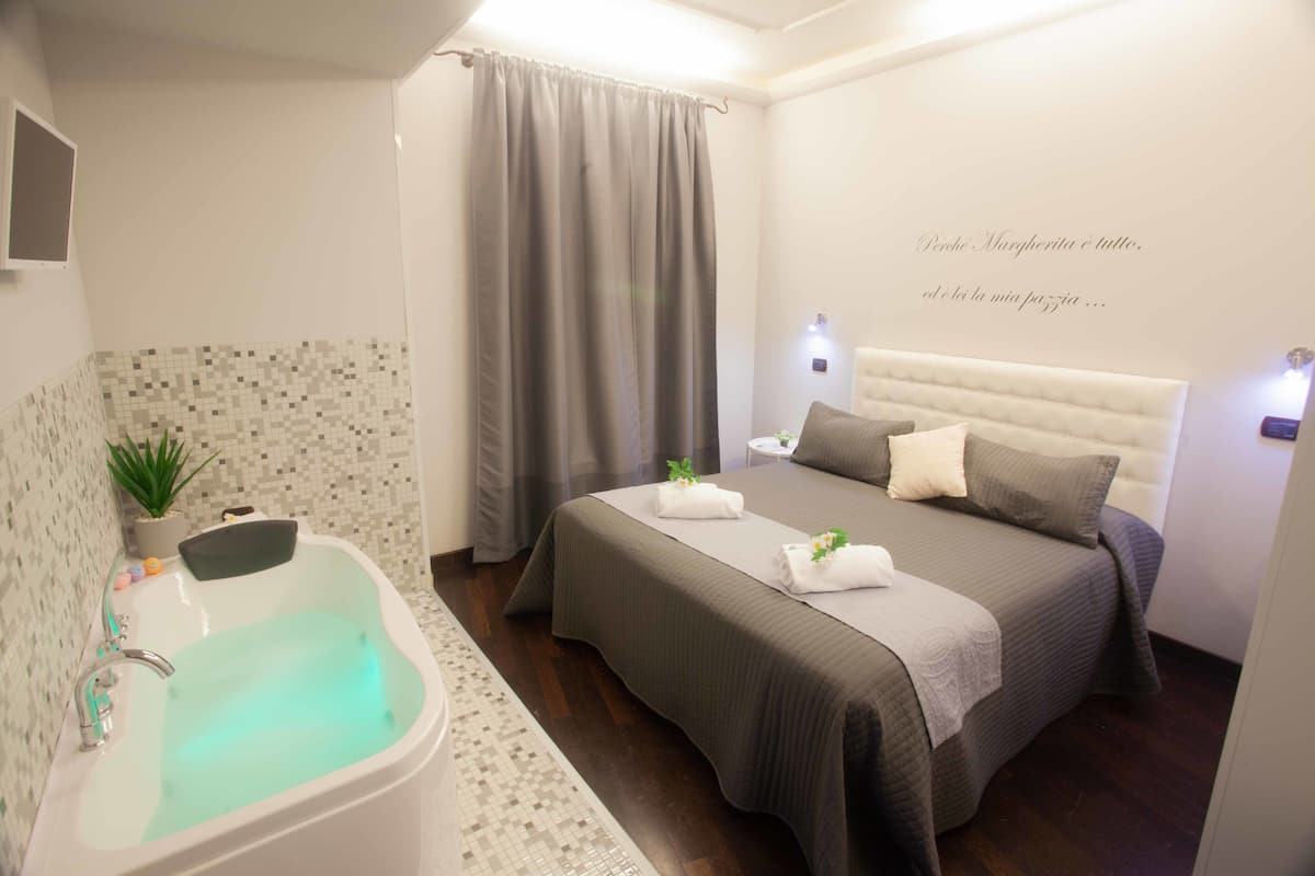 A modern hotel room with a large bed, a bathtub, and a small bedside table.