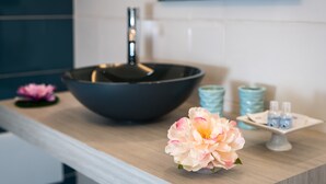 Un tocador de baño con un lavabo negro, una flor rosa y dos jarrones azules.