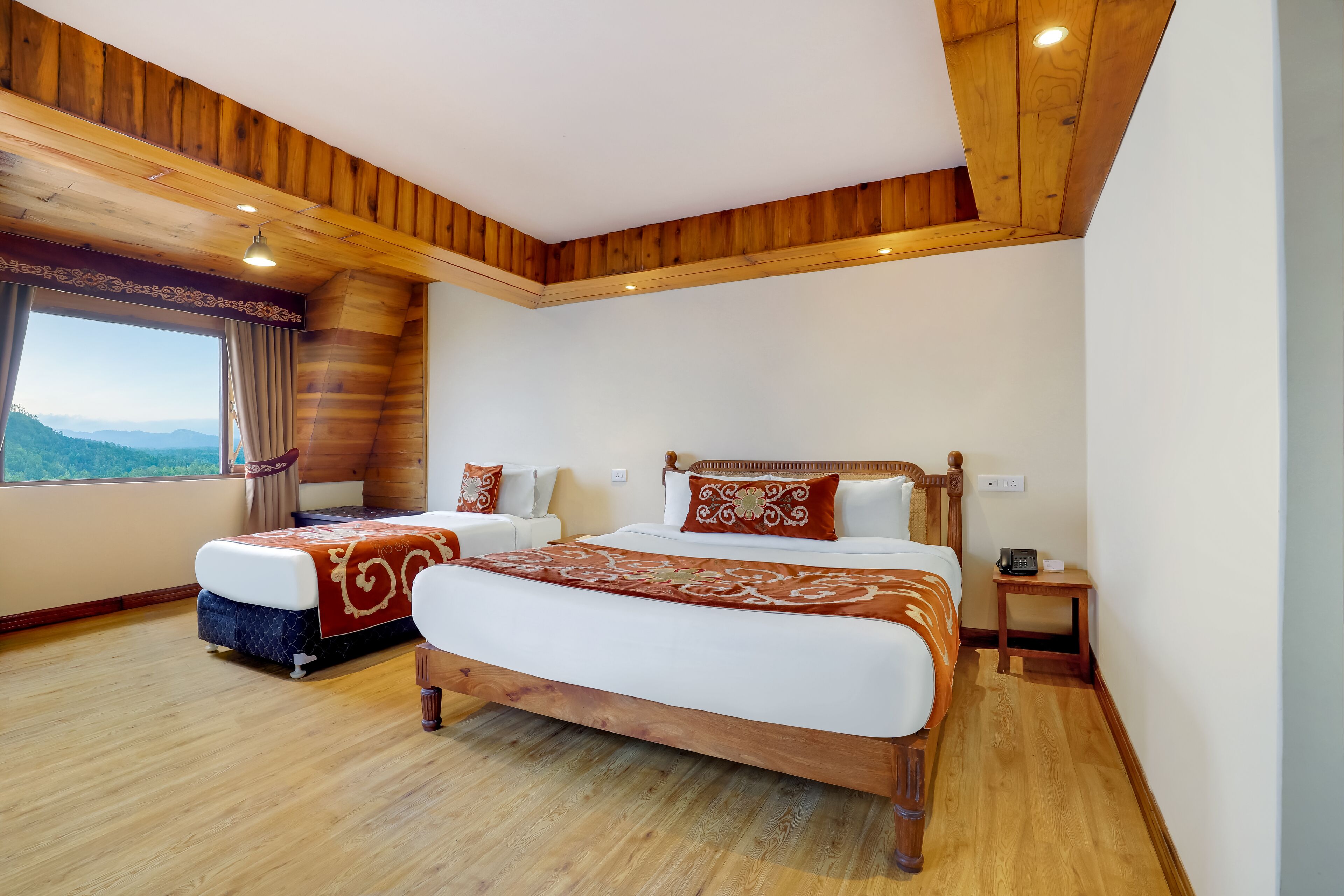 A bedroom with two beds, wooden ceiling, large window with curtains, and a view of the mountains.