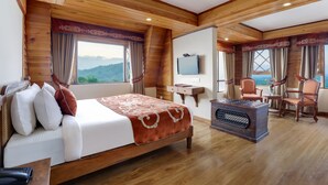 A wooden-paneled room with a bed, a television, and a seating area with chairs and a table. - Summit Hermon Hotel & Spa (Darjeeling)