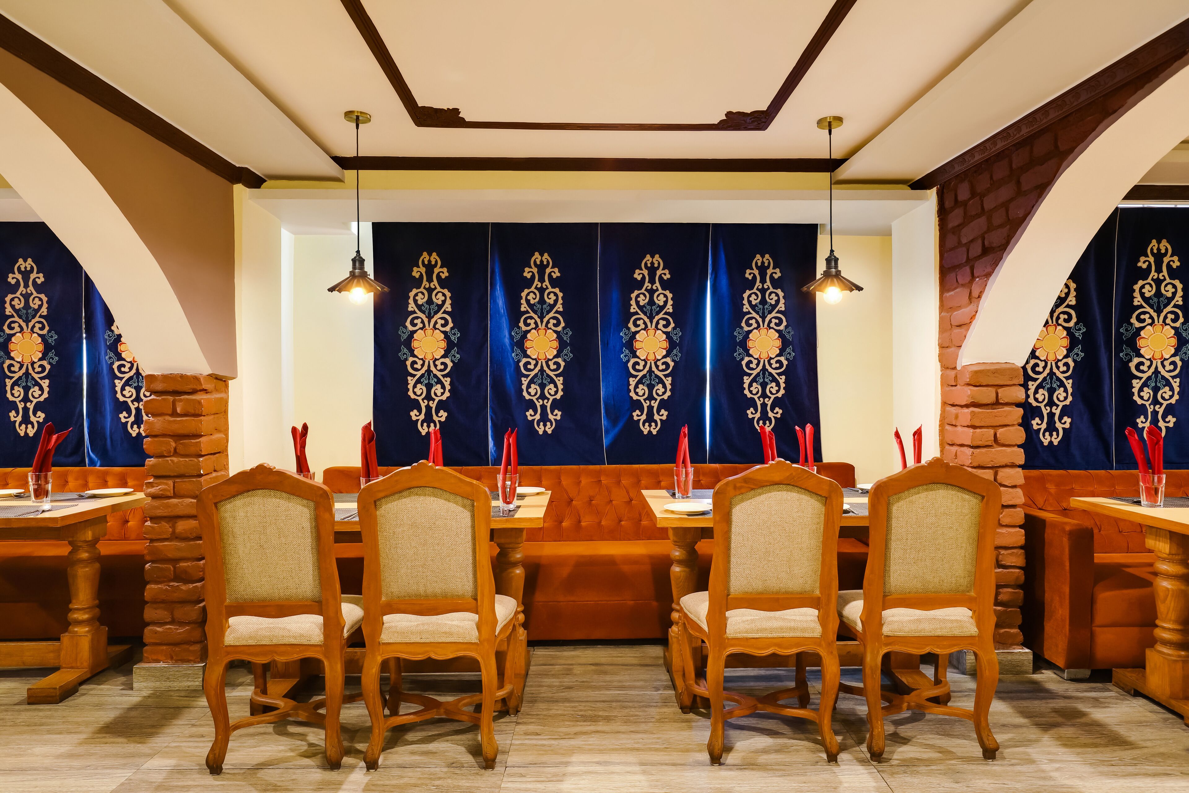 Un restaurante con mesas y sillas de madera, cortinas azules con diseños dorados y una pared de ladrillo.