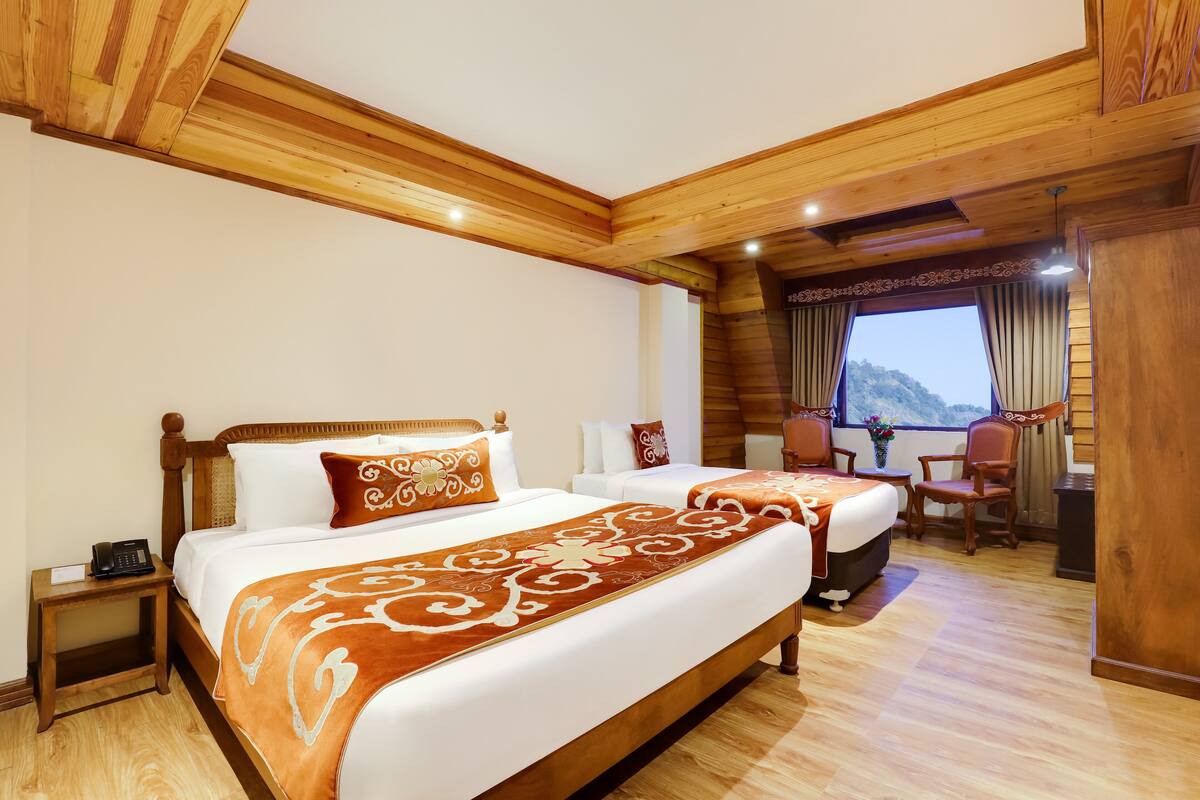 Une chambre d’hôtel avec deux lits, des poutres en bois au plafond, un petit bureau et une fenêtre donnant sur une vue sur la montagne.