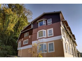 Un edificio de varios pisos con fachada marrón y beige, múltiples ventanas de marco blanco y techo inclinado.