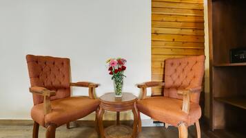 Dos sillones tapizados con reposabrazos y patas de madera, una mesita redonda de madera con un centro tejido, y un jarrón con flores sobre la mesa.