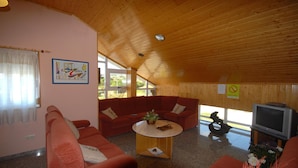 Un salon chaleureux avec un plafond en bois, des canapés rouges, une table basse et un téléviseur.