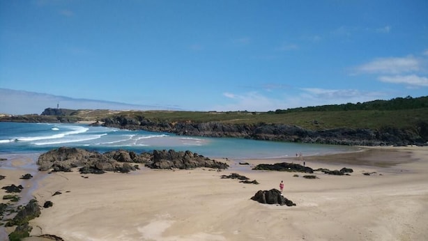 Une plage avec des affleurements rocheux, une eau calme et un ciel dégagé.