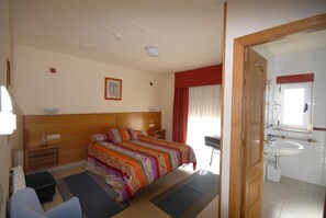 A hotel room with a large bed, a bedside table, a chair, a small table, a mirror, and a bathroom with a sink and toilet. - Hotel Valdoviño Express (Valdovino)