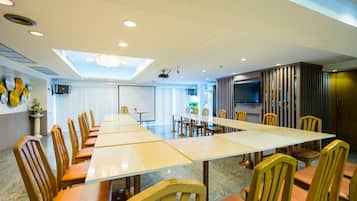 Ein Konferenzraum mit langem Tisch und Stühlen, einem Projektor und einem Fernseher an der Wand.