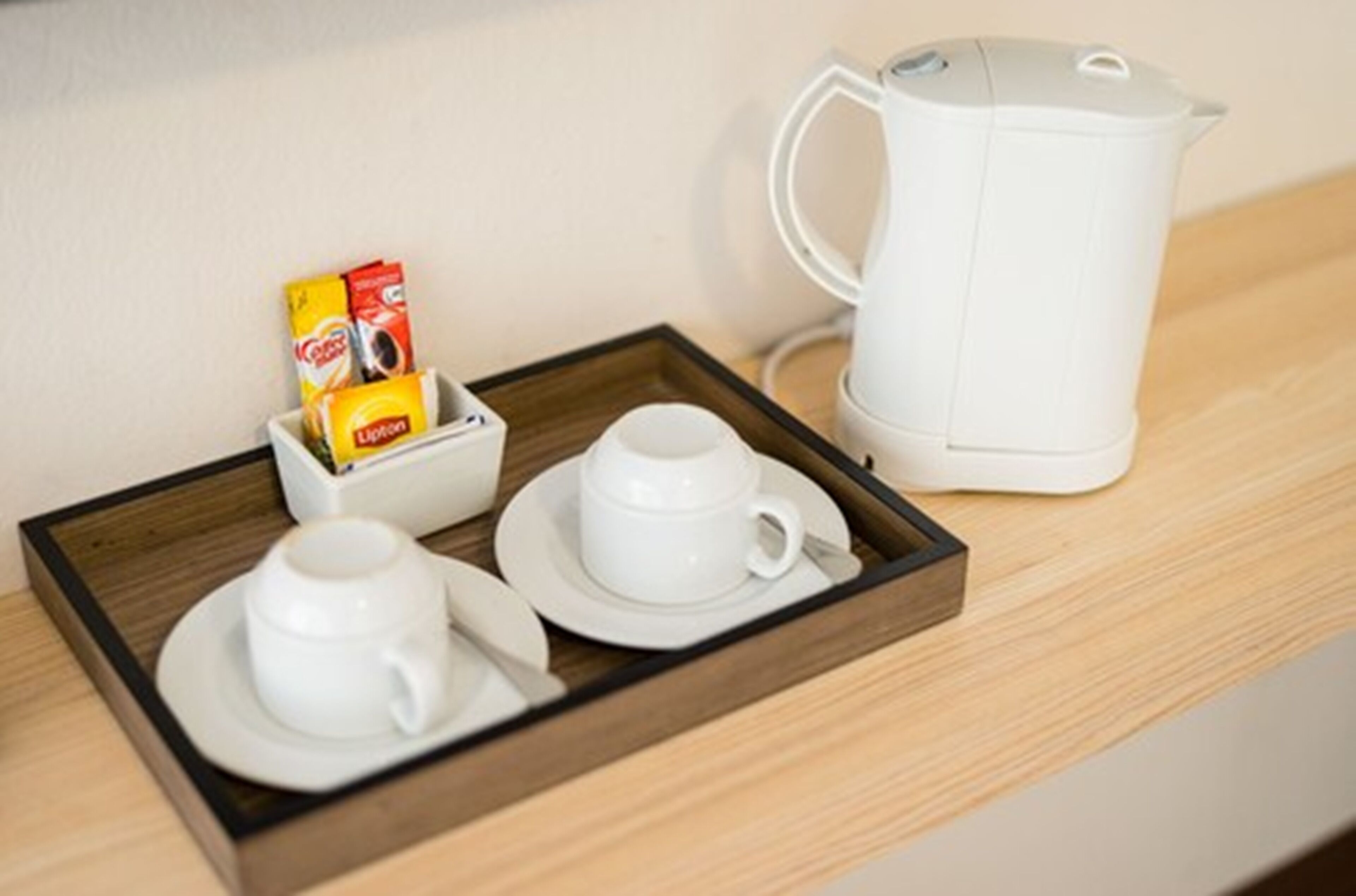 A tray with two white cups and a box of Lipton tea, and a white electric kettle on a wooden surface.