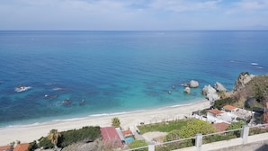 A coastal view with a beach, rocky outcrops, and a few buildings. - Borgo degli Dei - Affittacamere Poseidone (Parghelia)