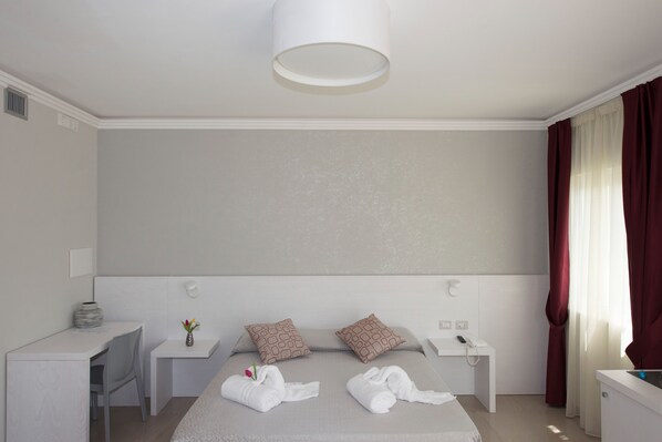 A modern hotel room with a bed, bedside tables, a desk, and a lamp.