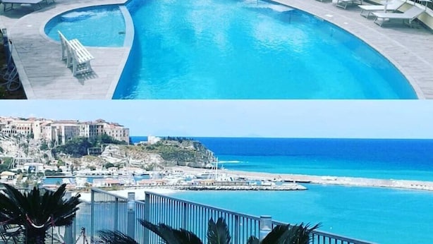 A pool with lounge chairs and umbrellas, surrounded by trees and overlooking a coastal area with buildings and a pier. - Borgo degli Dei - Affittacamere Poseidone (Parghelia)