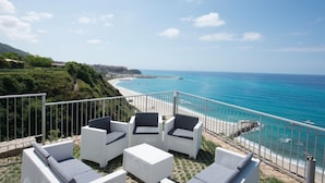 A balcony with white wicker furniture and a view of the beach and ocean. - Borgo degli Dei - Affittacamere Poseidone (Parghelia)