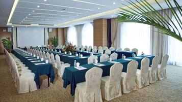 A conference room with rows of tables, chairs, and a large screen.