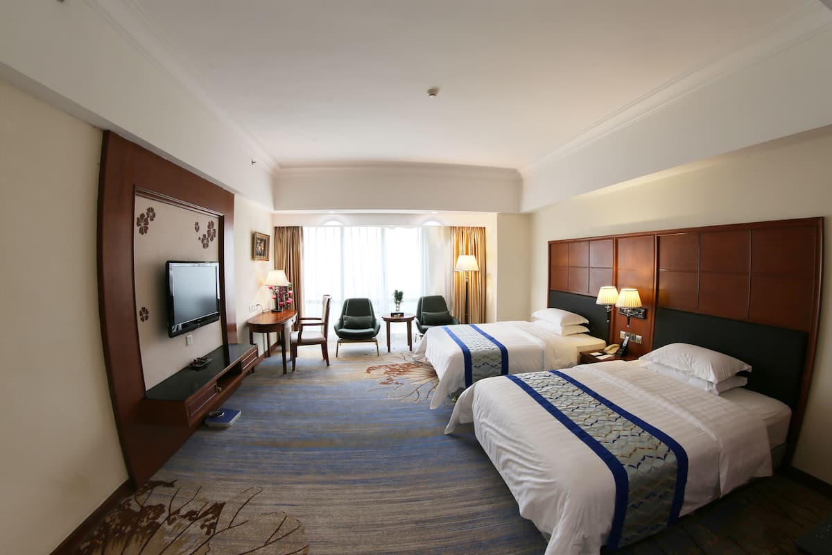 A hotel room with two beds, a TV, a desk with a chair, and a view of the outdoors.