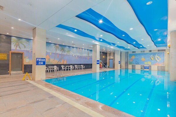 An indoor swimming pool with clear lane markings, a mural depicting a beach scene, and a ceiling with blue wave patterns. - Jiangmen Gladden Hotel (Jiangmen)