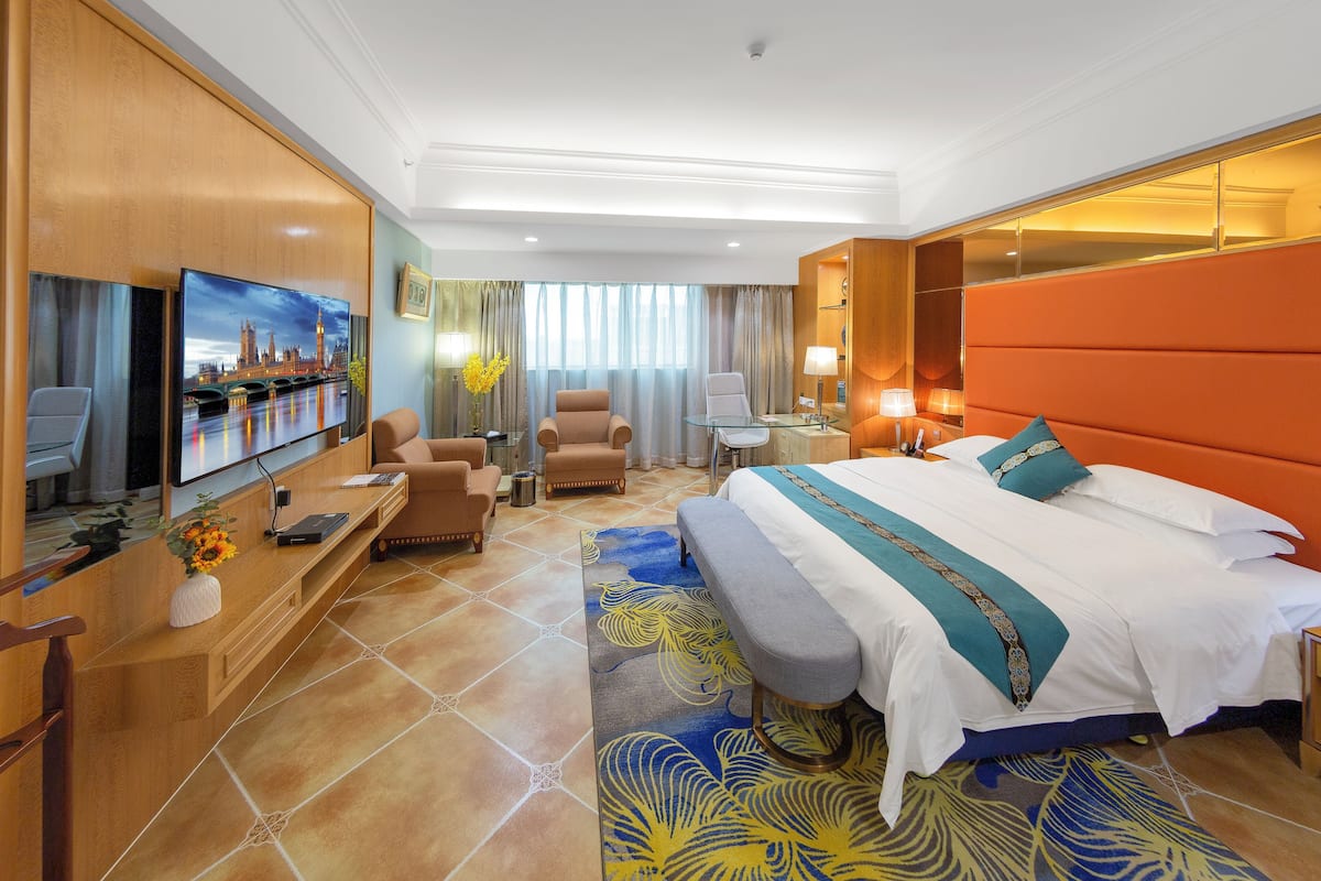 A hotel room with a large bed, a desk with a flat-screen TV, a sofa, and a chair.