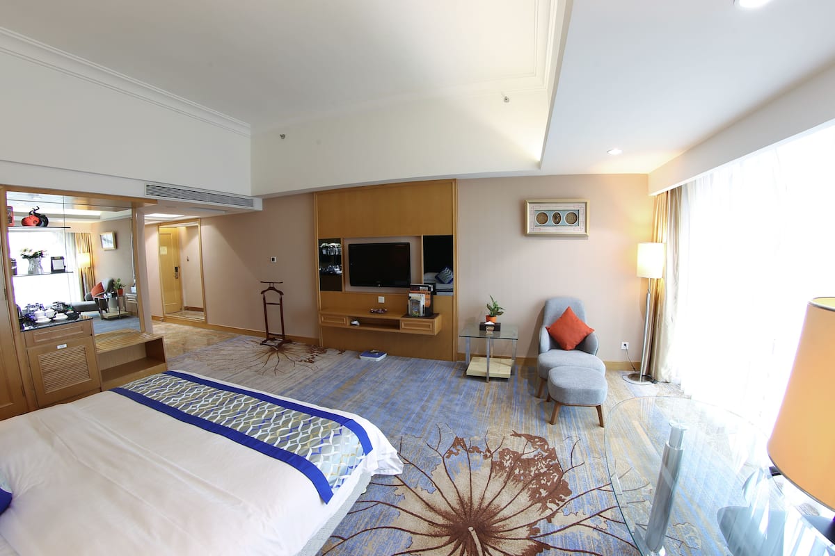 A hotel room with a large bed, a TV, a chair, a desk, and a mirror.
