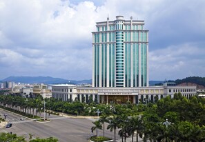 A tall hotel with a central tower, surrounded by palm trees and a wide road. - Jiangmen Gladden Hotel (Jiangmen)