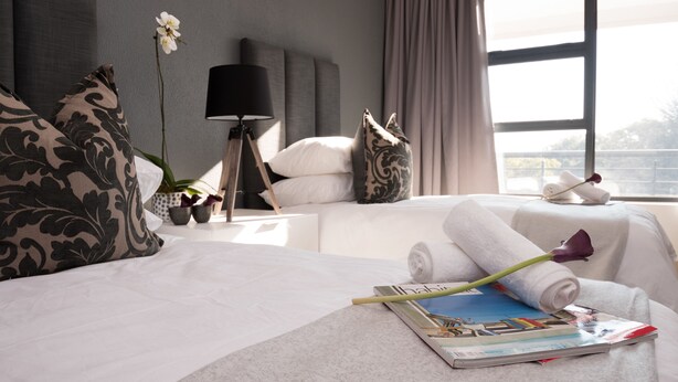 Een hotelkamer met een netjes opgemaakt bed, een nachtkastje met een lamp, een raam met gordijnen en uitzicht op de omgeving.