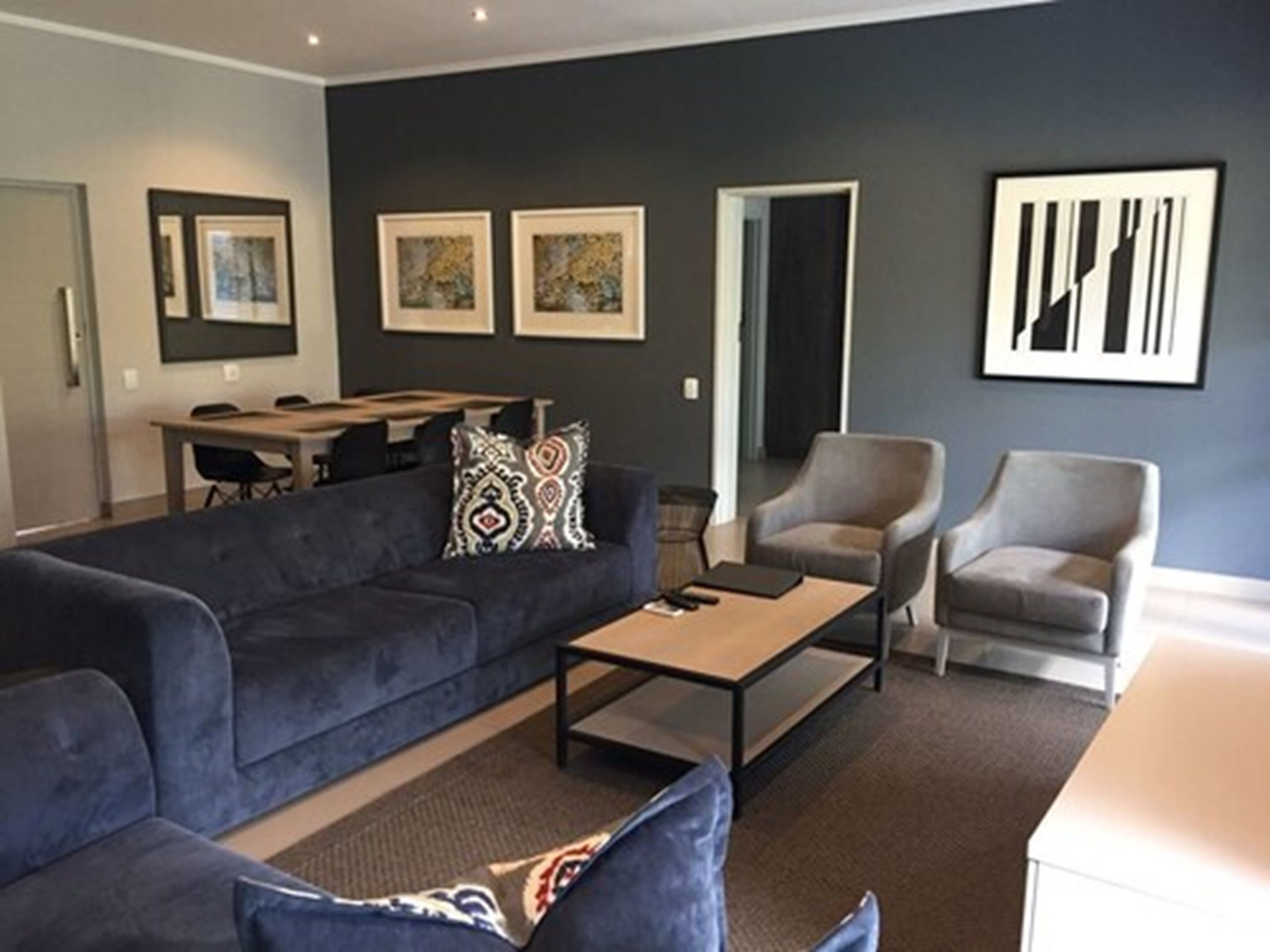 A modern living room with a dark blue sofa, two armchairs, a coffee table, and a dining area with a table and chairs.